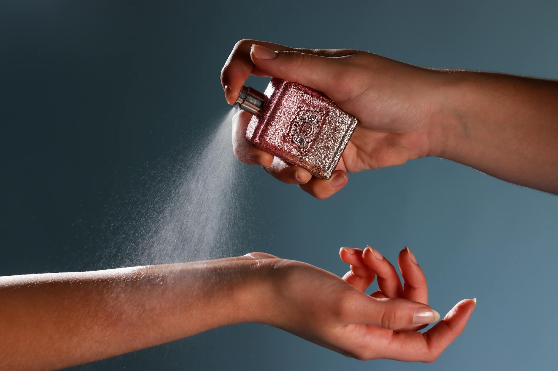 Dłoń spryskująca nadgarstek mgiełką na niebieskim tle