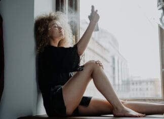 Kobieta przy oknie rozpyla na włosy nawilżający spray przeciw puszeniu