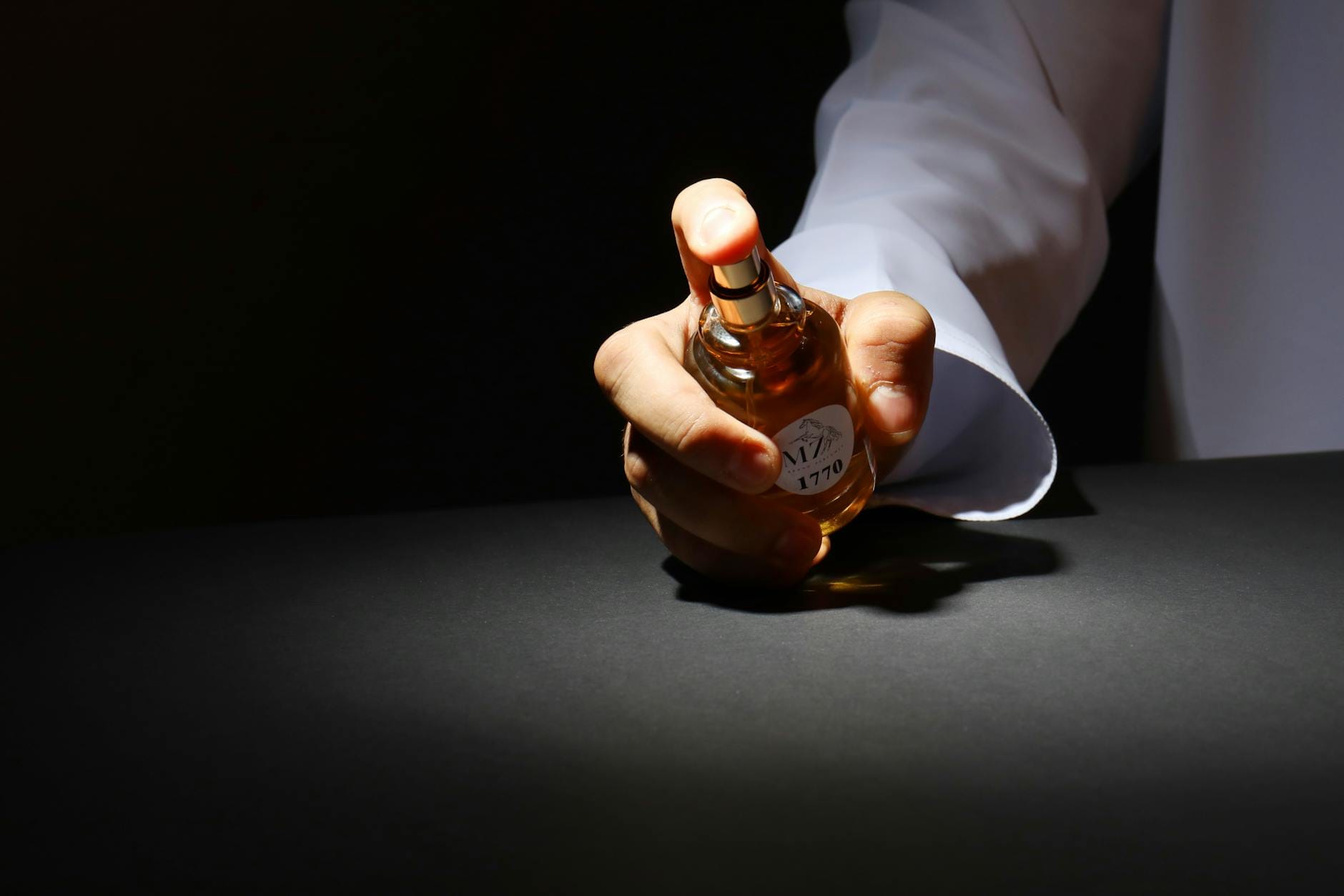 Dłoń trzymająca elegancki flakon perfum na ciemnym tle