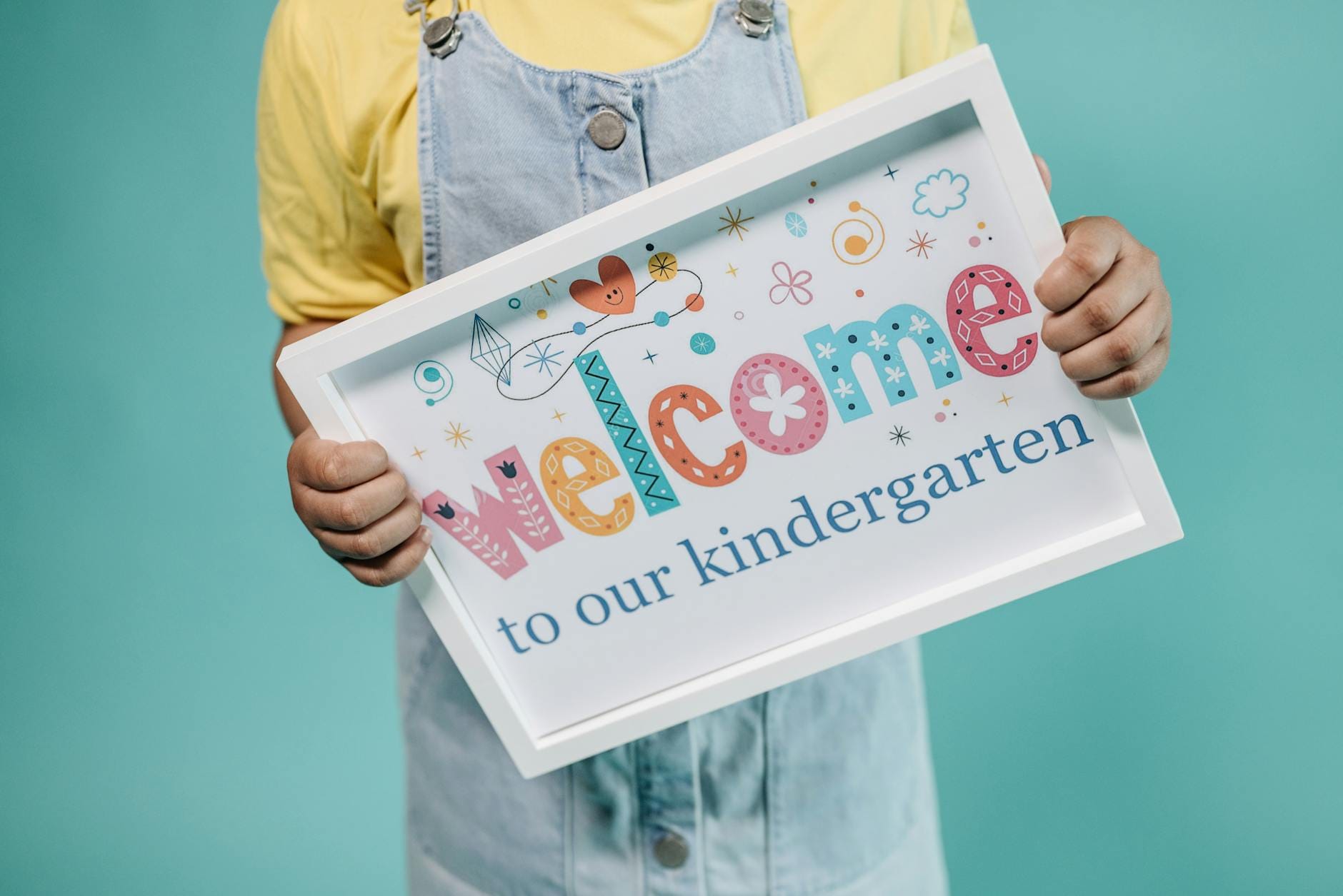 Dziecko trzyma kolorowy plakat welcome to kindergarten na turkusowym tle