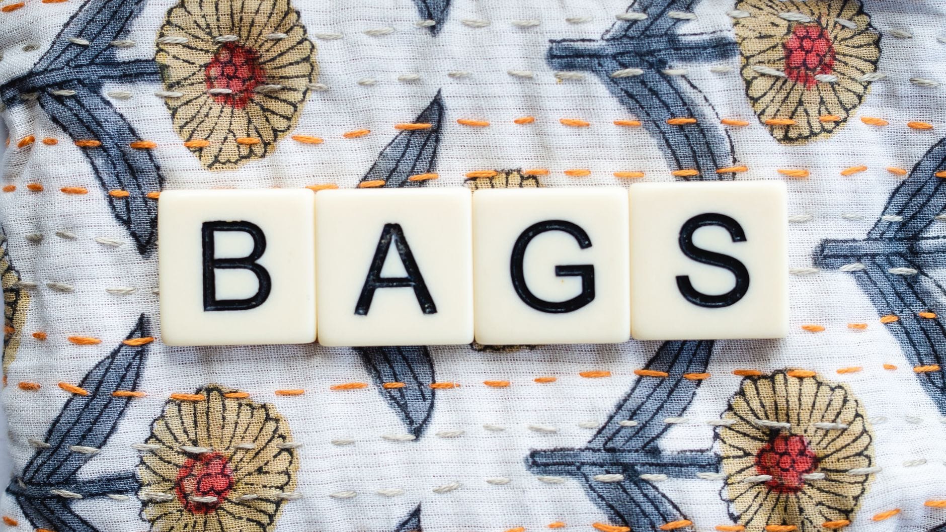 Zbliżenie na litery z napisu BAGS na haftowanym kwiecistym materiale