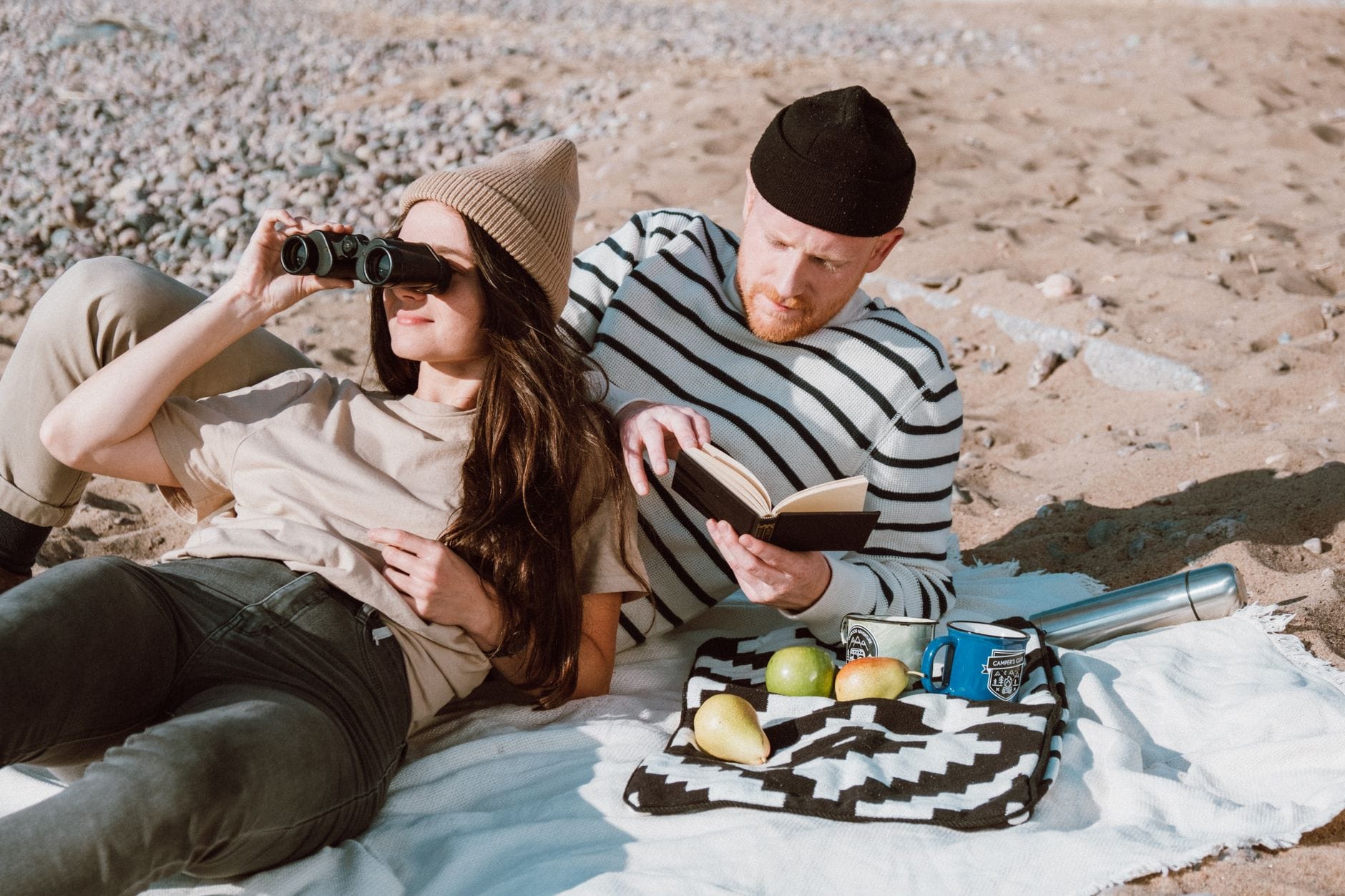 Para odpoczywa na plaży z przekąskami, książką i lornetką